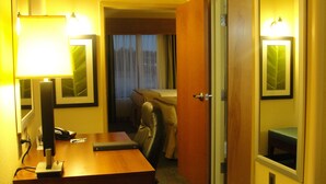 A hotel room with a wooden desk, a chair, a bed, and a door leading to another room. - Holiday Inn Express & Suites Atlanta East – Lithonia by IHG (Lithonia)