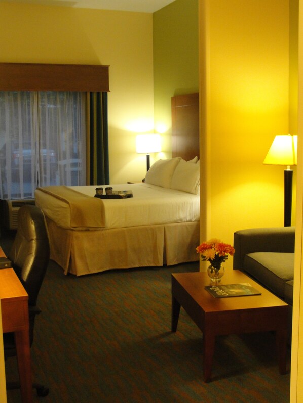 A hotel room with a bed, a desk, a chair, a lamp, and a vase with flowers. - Holiday Inn Express & Suites Atlanta East – Lithonia by IHG (Lithonia)