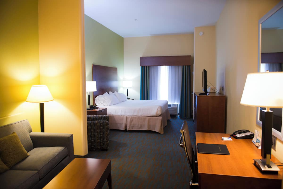 A hotel room with a bed, a desk, a chair, a sofa, and a lamp.