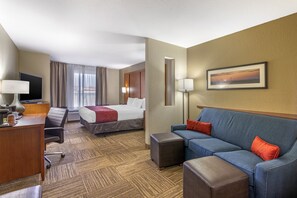 Habitación de hotel con cama, escritorio con lámpara, sofá e imagen enmarcadas en la pared.