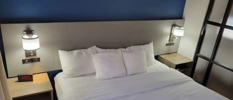 Una habitación de hotel con una cama, dos mesitas de noche, un reloj digital y lámparas de pared.
