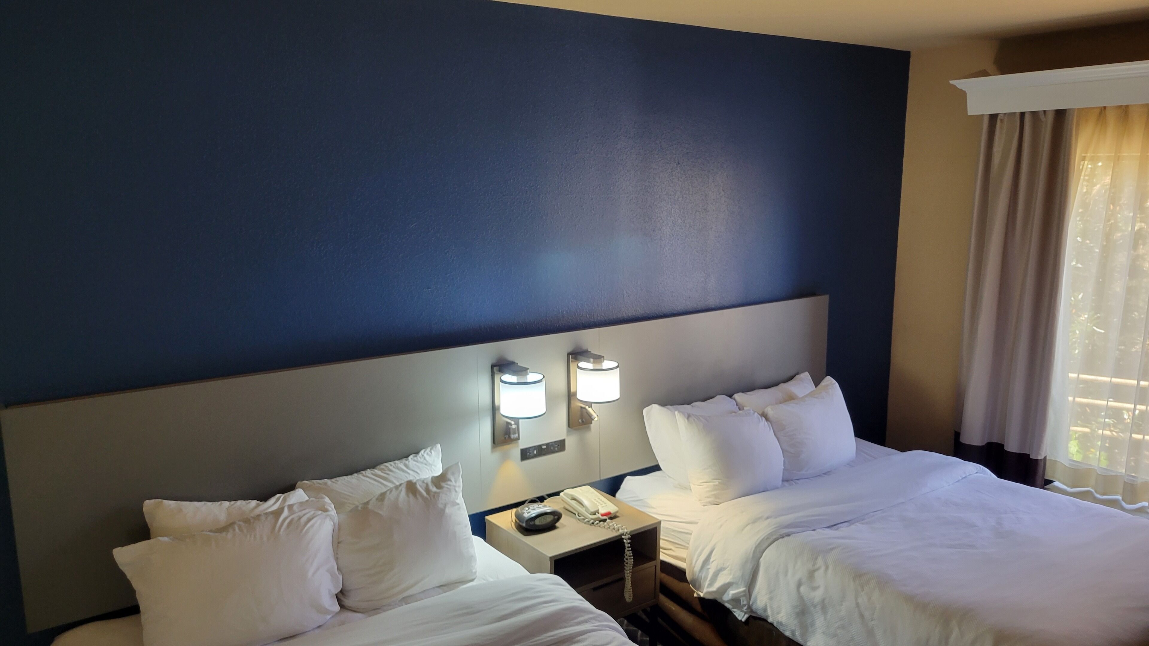 A hotel room with two beds, a nightstand with a phone, and wall-mounted lamps.