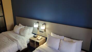 Habitación de hotel con dos camas, cada una con ropa de cama y almohadas blancas. Hay dos mesitas de noche, una de ellas con lámpara y teléfono.