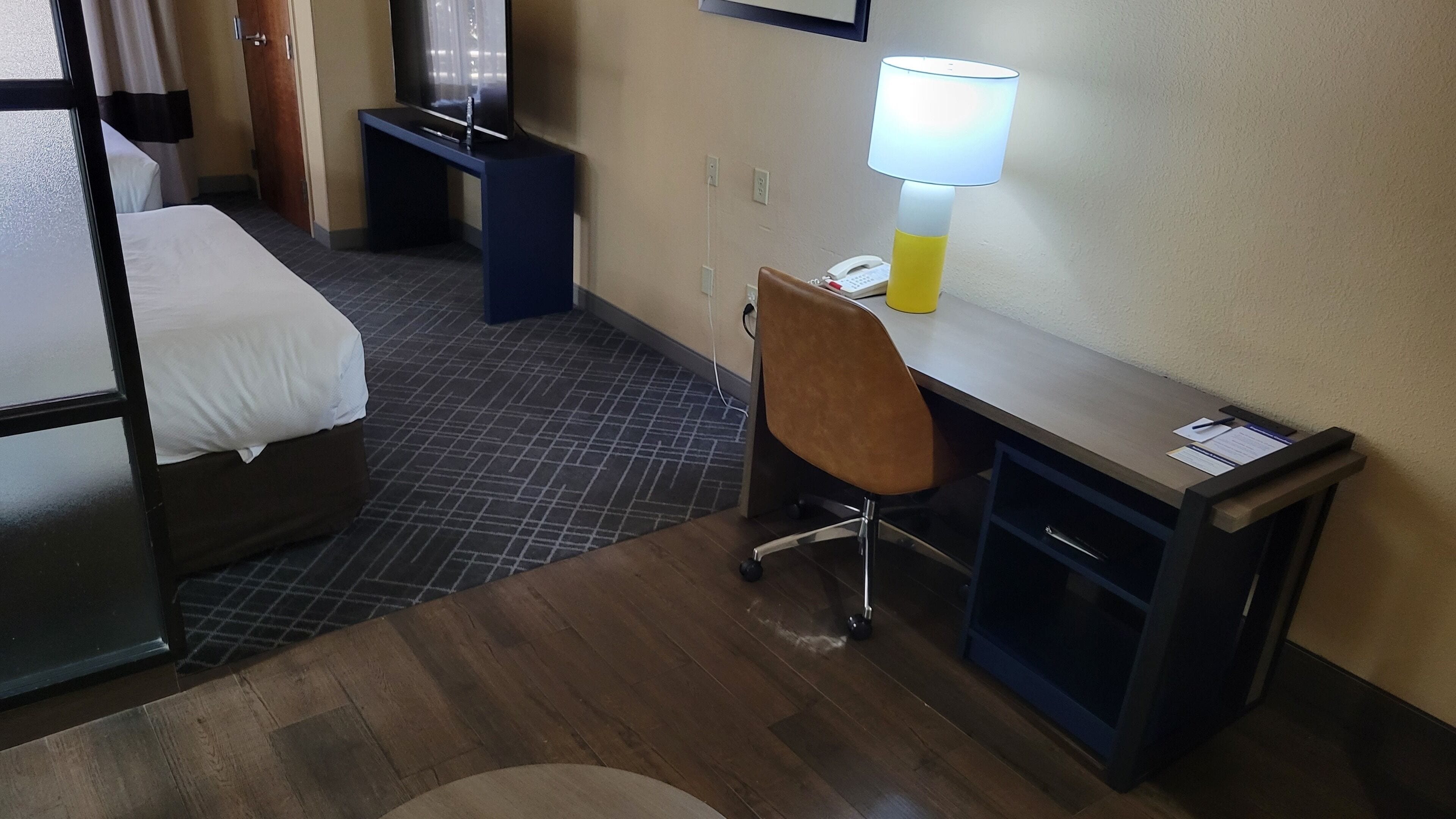 A hotel room with a bed, a desk with a chair, a lamp, and a phone.
