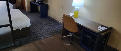 A hotel room with a bed, a desk with a chair, a lamp, and a phone.
