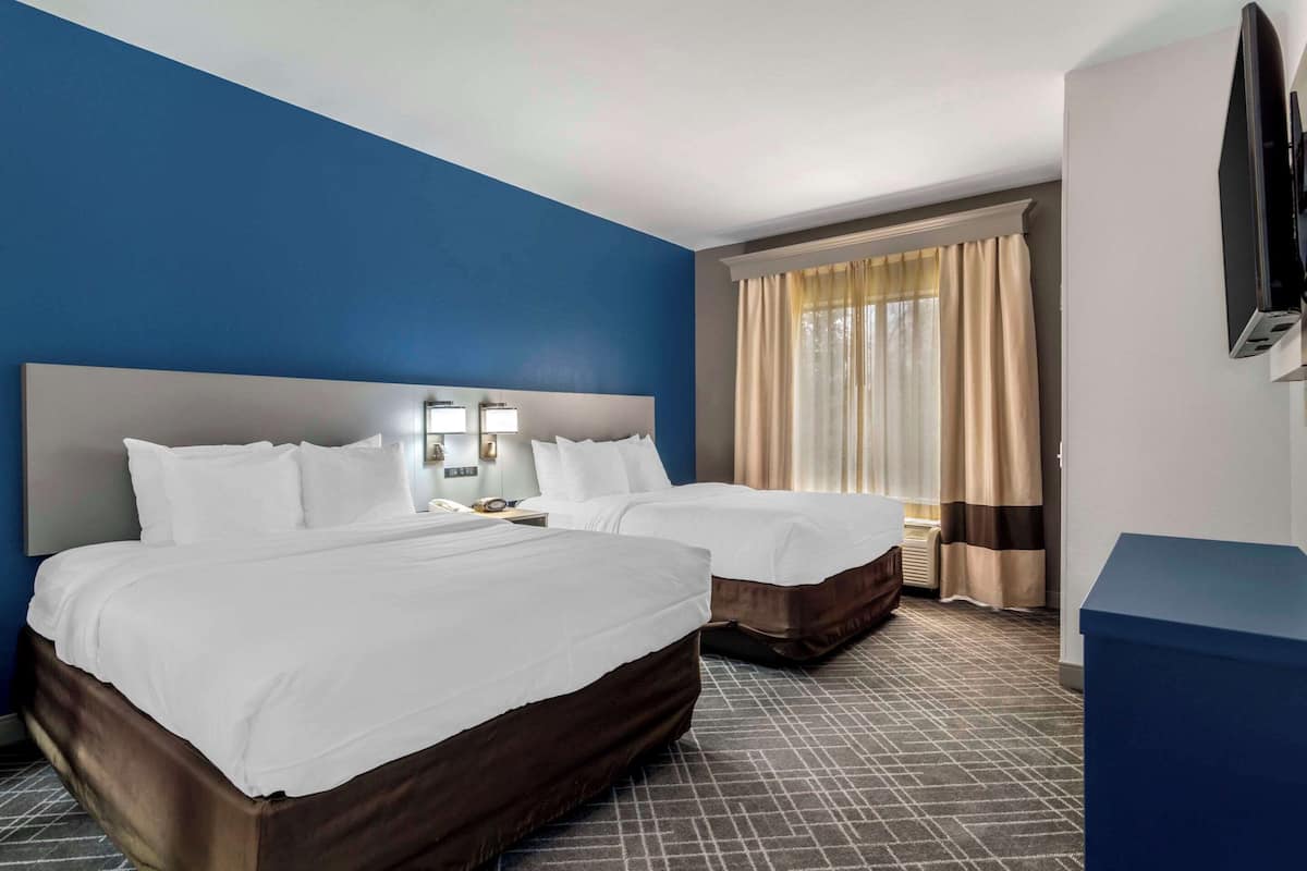 Ein Hotelzimmer mit zwei Betten, einem großen Flachbildfernseher, einem Nachttisch und einem Fenster mit Vorhängen.
