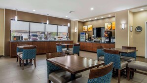 A restaurant with booths and tables, a counter with food and drinks, and a kitchen in the background. - Comfort Suites Macon Northwest (Macon)