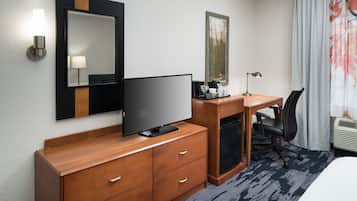 Habitación de hotel con escritorio de madera, televisor de pantalla plana, espejo, cuadro enmarcado, silla y cama.