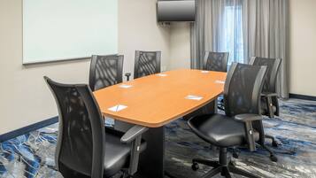A conference room with a long table, six chairs, a projector screen, and a TV.