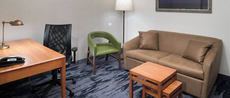 Una habitación con un escritorio de madera, una silla verde, un sofá marrón y una pequeña mesa de madera.