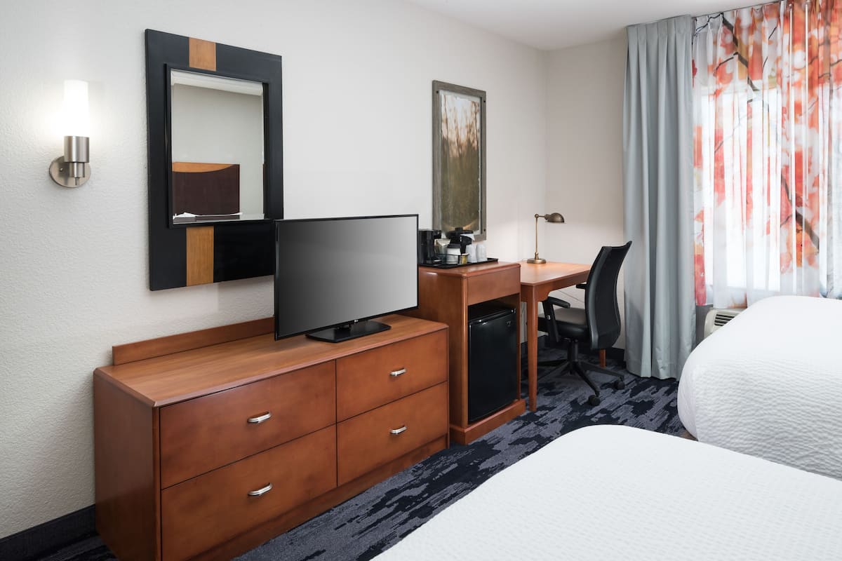 Habitación de hotel con cama, escritorio con computadora, televisor, cafetera y espejo.