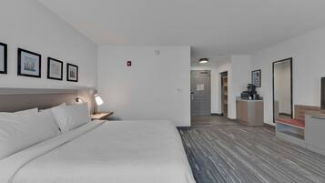 A hotel room with a large bed, a desk with a chair, a mirror, and framed pictures on the wall.