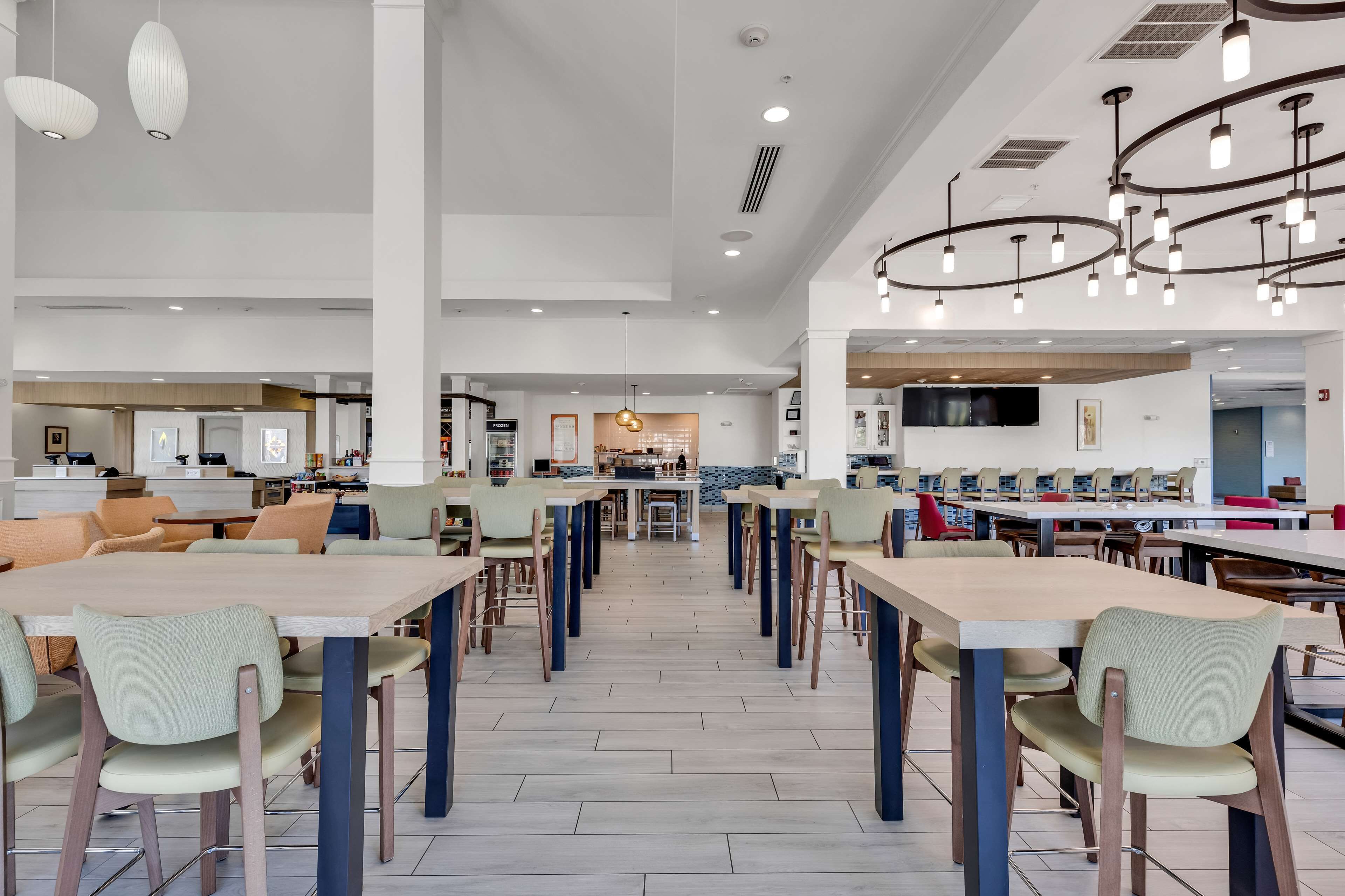 A spacious dining area with multiple tables and chairs, a central serving station, and modern lighting fixtures.