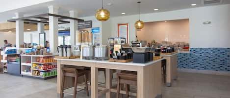 A modern cafe with a central island, bar stools, and a variety of food and drink items on display.