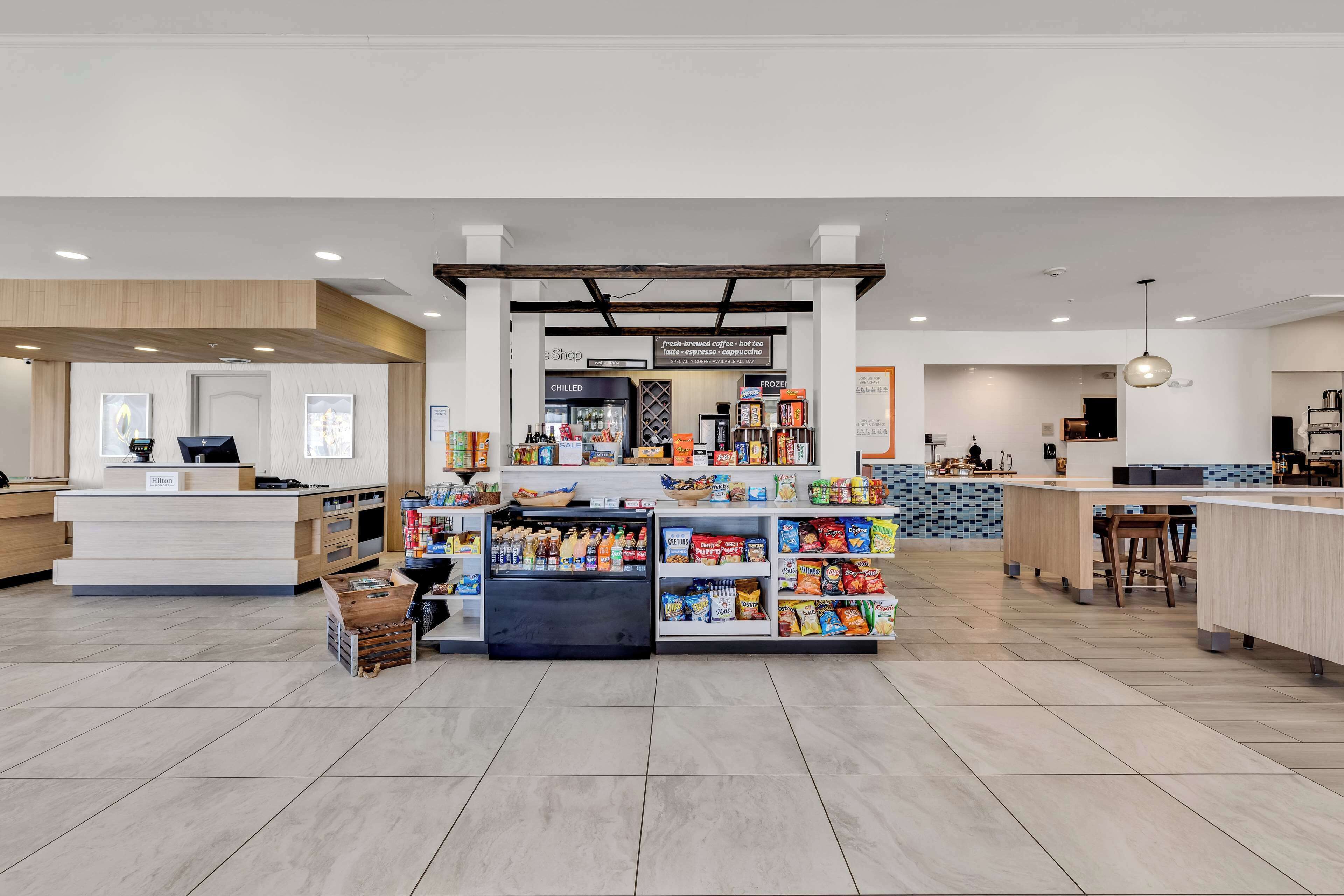 A hotel lobby with a reception desk, a coffee shop area, and a seating area with a counter.