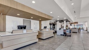 A modern hotel reception area with a wooden reception desk, a digital check-in station, and a clean, tiled floor. - Hilton Garden Inn Myrtle Beach/Coastal Grand Mall (Myrtle Beach)