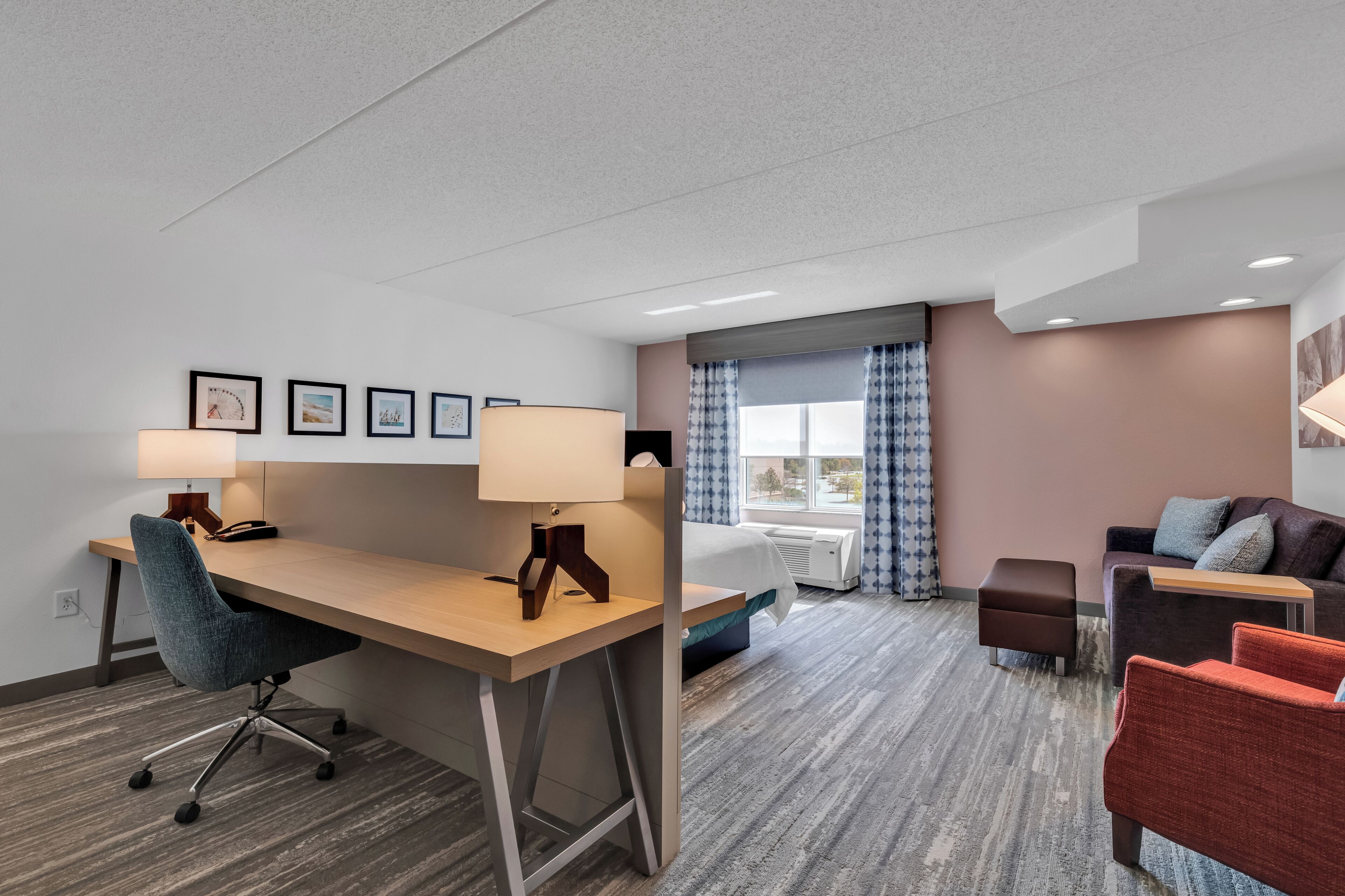 A hotel room with a wooden desk, a blue office chair, a brown sofa, and a red armchair.