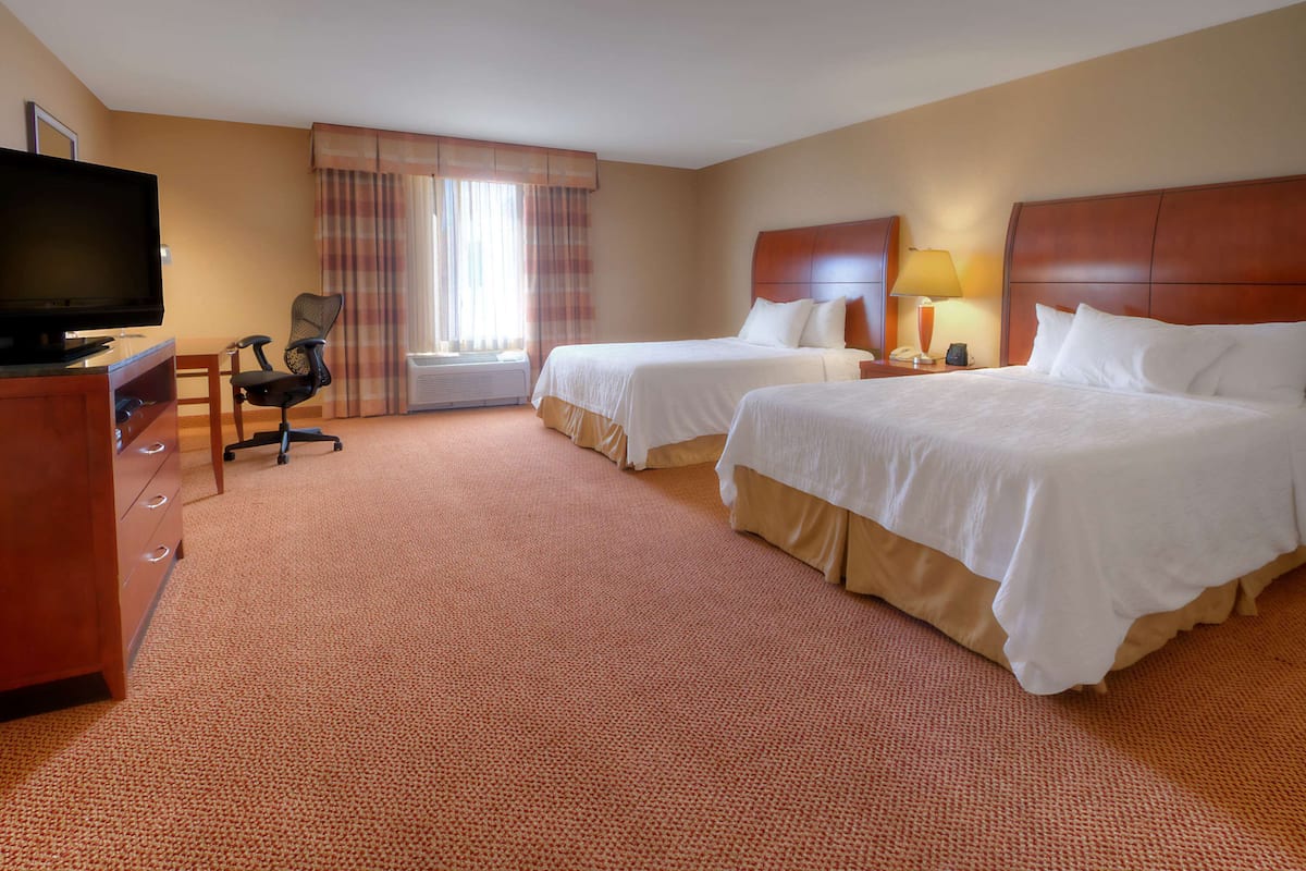 A hotel room with two beds, a desk with a chair, a television, and a window with curtains.