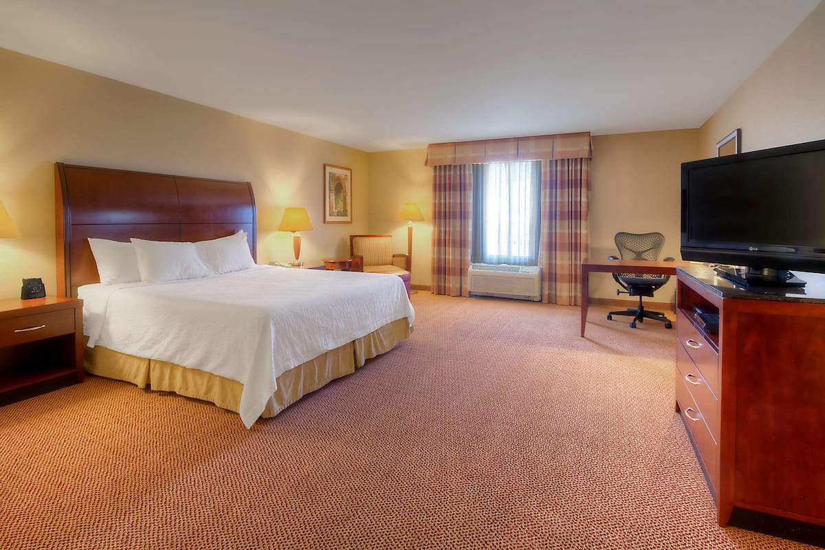 A hotel room with a large bed, a desk with a television, and a chair.