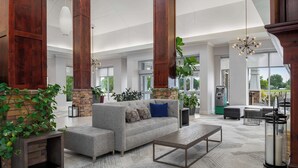 A spacious living area with a grey sofa, a coffee table, and a stone accent wall. There are large windows, a fireplace, and various plants.