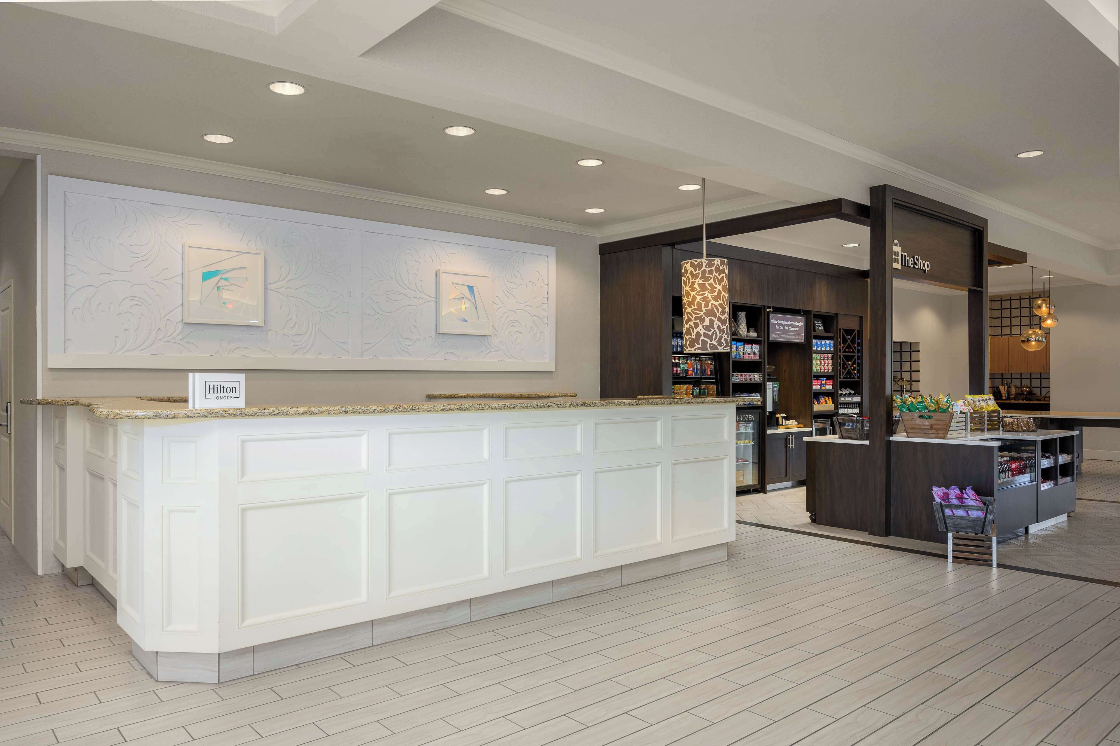 A hotel reception area with a white counter, a 'Hilton' sign, and a 'The Shop' section with various items.
