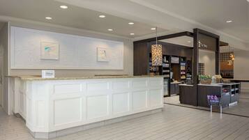 A hotel reception area with a white counter, a 'Hilton' sign, and a 'The Shop' section with various items.
