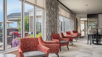 Un hall d’hôtel doté de grandes fenêtres, de fauteuils à motifs rouges et d’un espace bar.