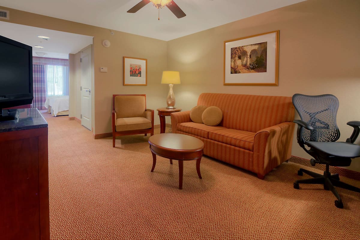 A hotel room with a television, a sofa, a chair, a small table, and a lamp.