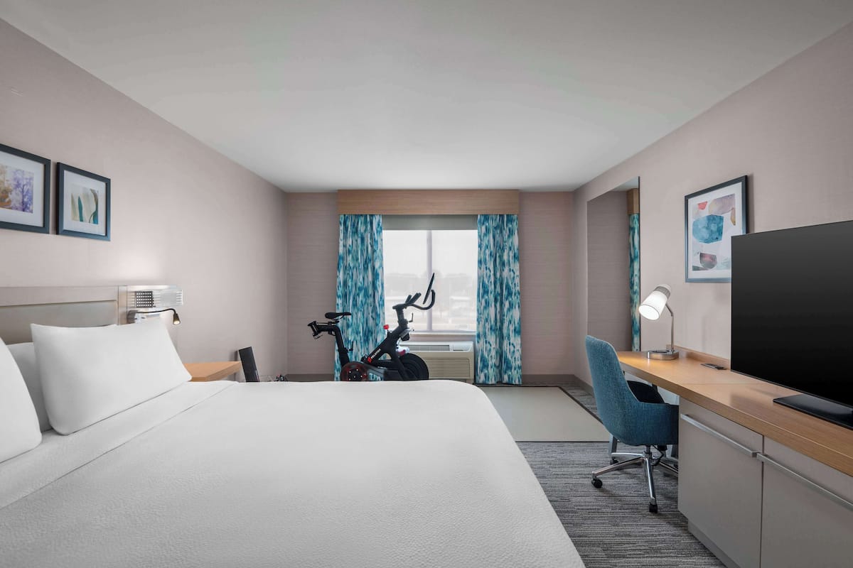 A hotel room with a bed, a desk with a TV, a bicycle, and a window with curtains.