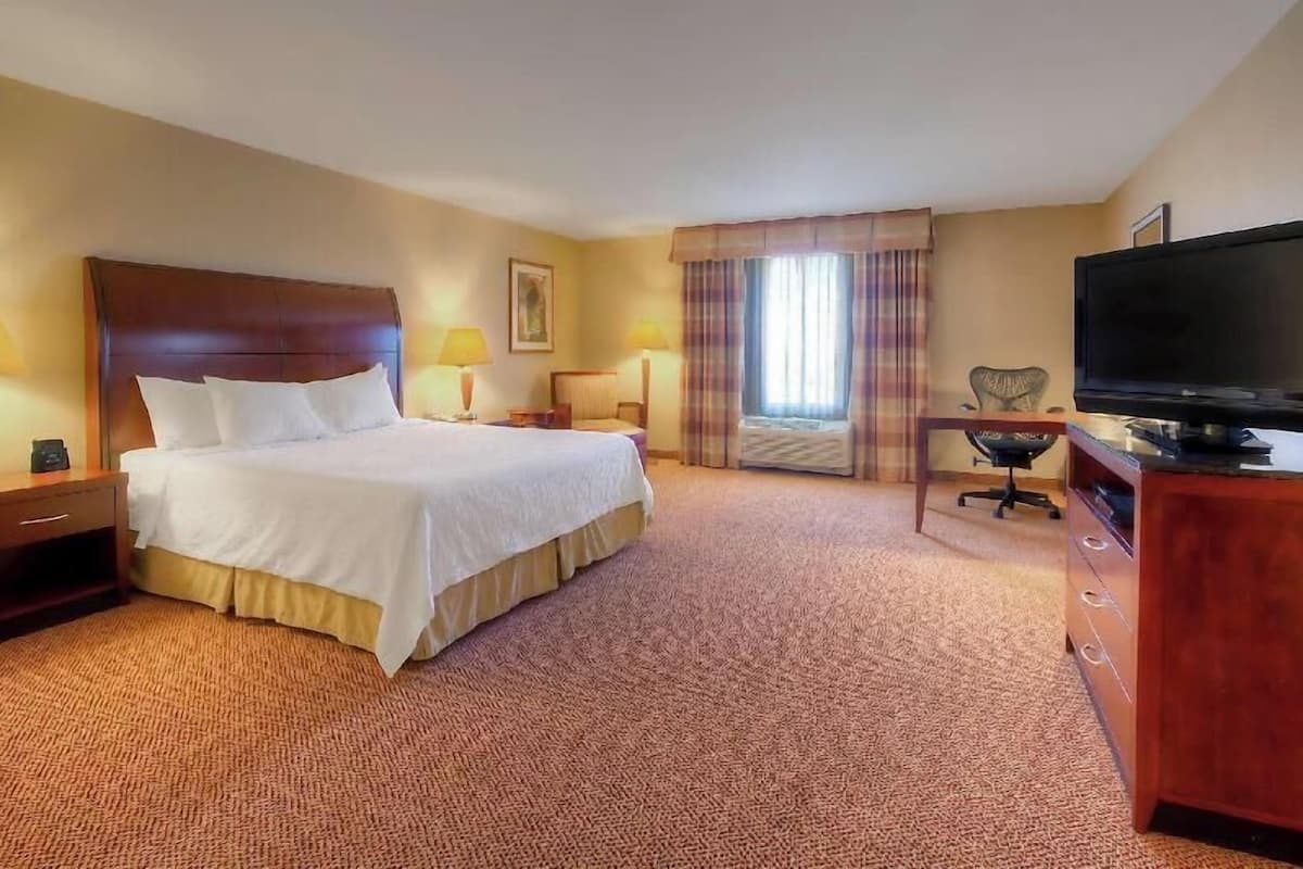 A hotel room with a large bed, a desk with a chair, a television, and a window with curtains.