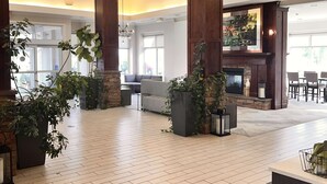 A spacious lobby with wooden flooring, large pillars, hanging pendant lights, and potted plants.