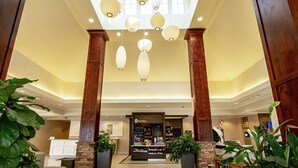 A hotel lobby with a reception desk, large potted plants, and a ceiling with hanging light fixtures.