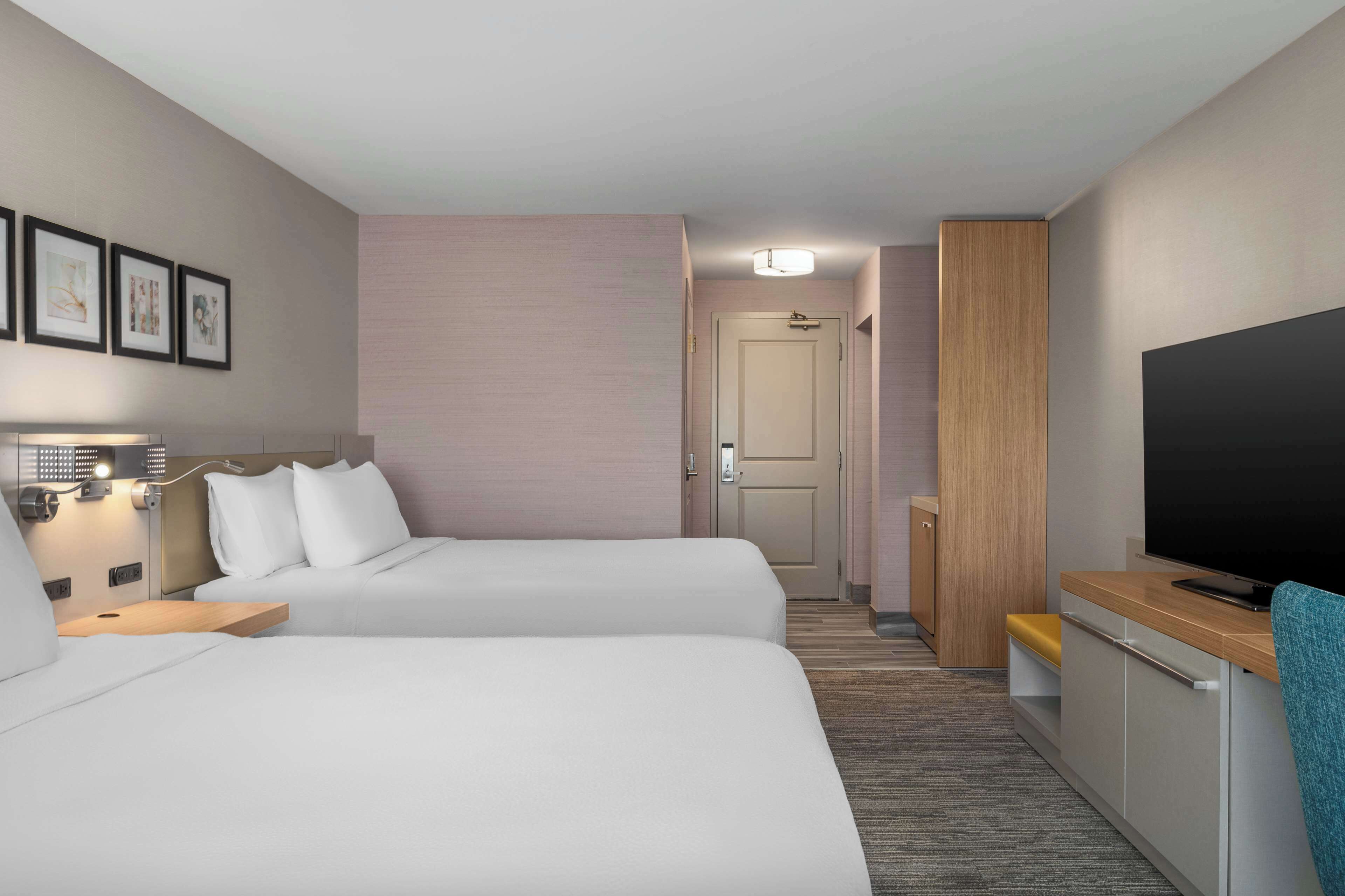 Une chambre d’hôtel avec deux lits, une télévision, un bureau et une porte donnant sur un couloir.