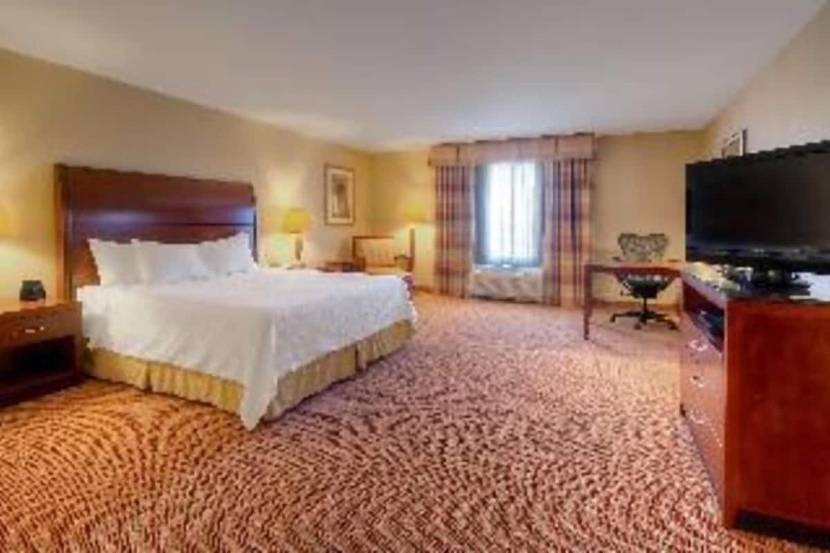 A hotel room with a bed, a television, a desk, and a window with curtains.