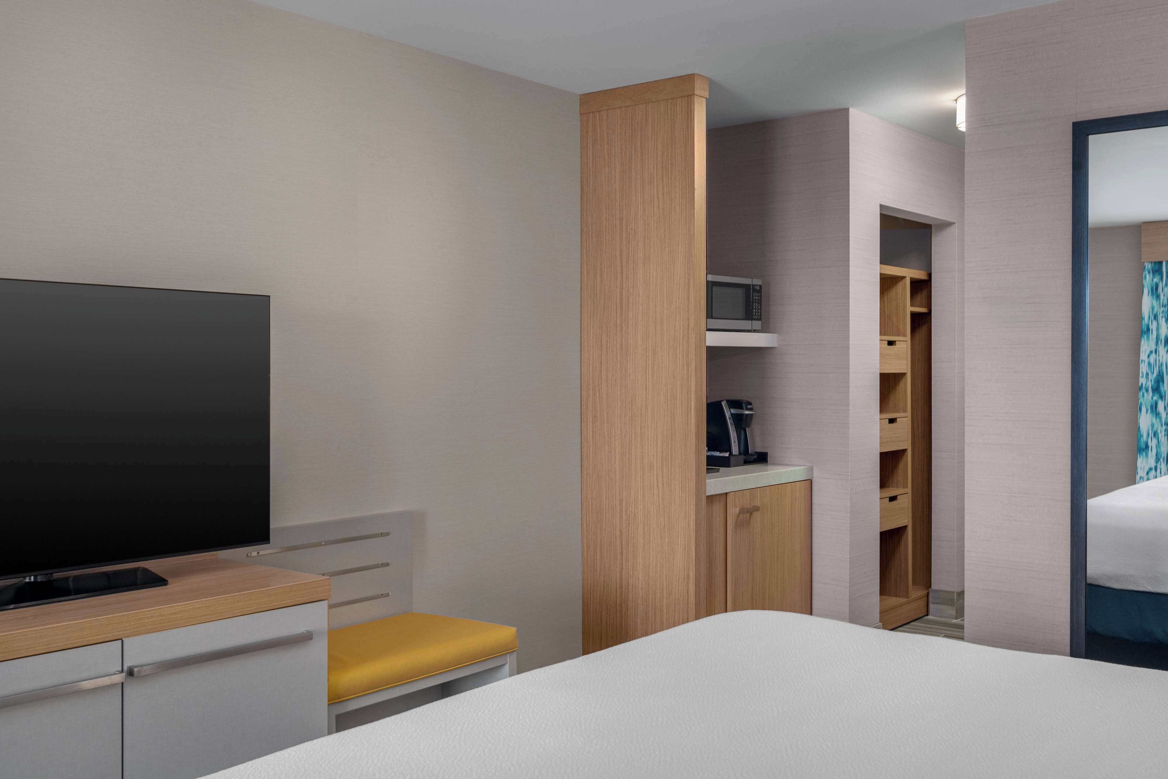 A modern hotel room with a flat-screen TV, a wooden cabinet, a microwave, and a bed.