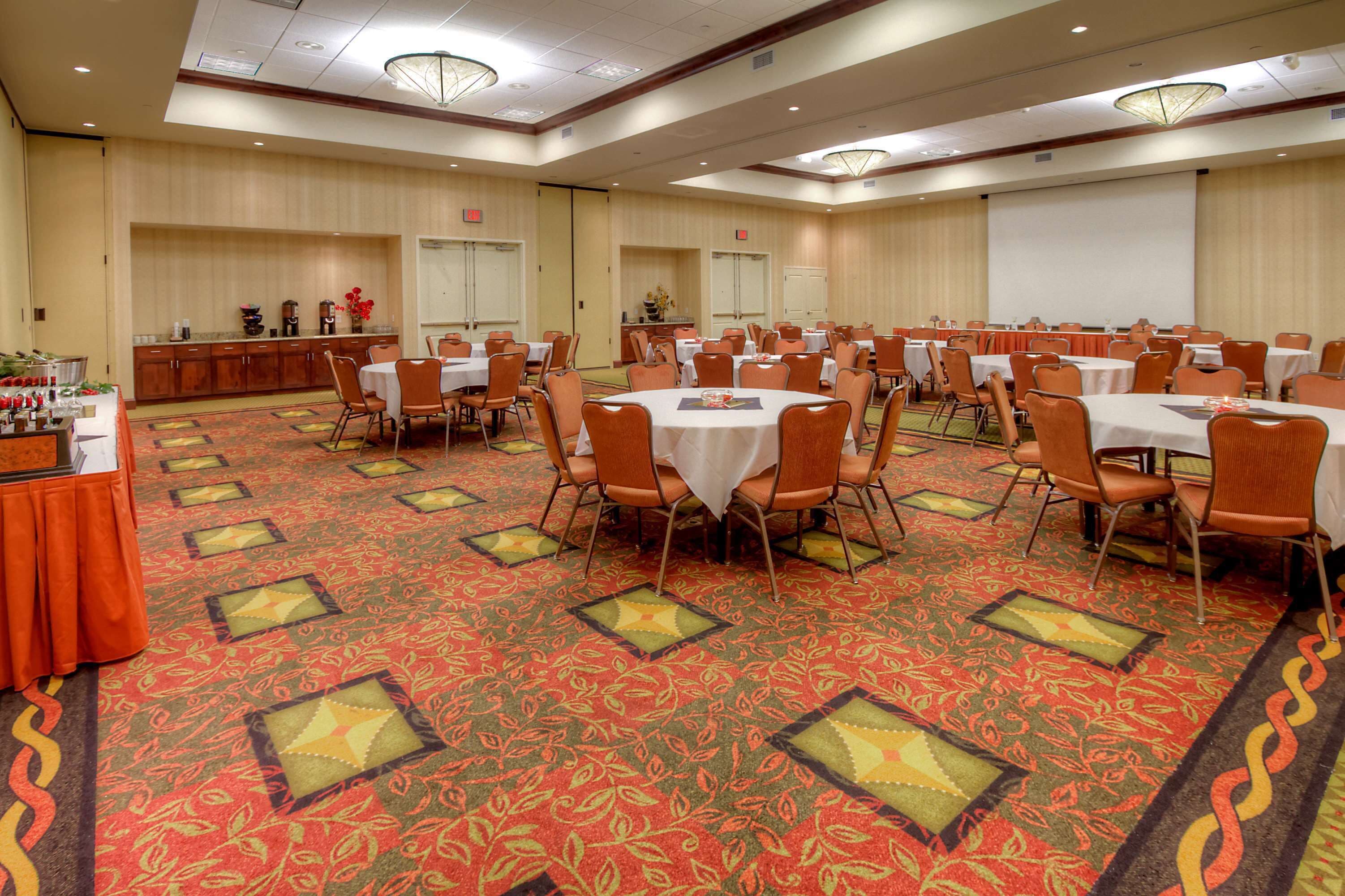 A large conference room with round tables and chairs, a buffet area, and a stage.