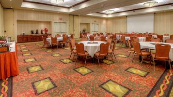 A large conference room with round tables and chairs, a buffet area, and a stage.