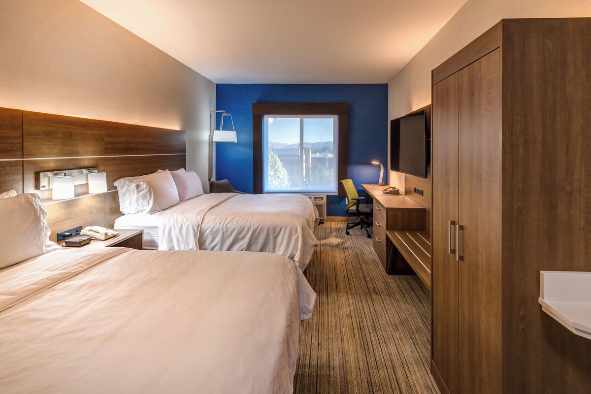 Habitación de hotel con dos camas, un escritorio, un televisor y un ventanal con vistas.