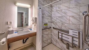 A modern bathroom with a shower, grab bars, a sink with a mirror, and a toilet paper holder. - Holiday Inn Express Reno Airport by IHG (Reno)