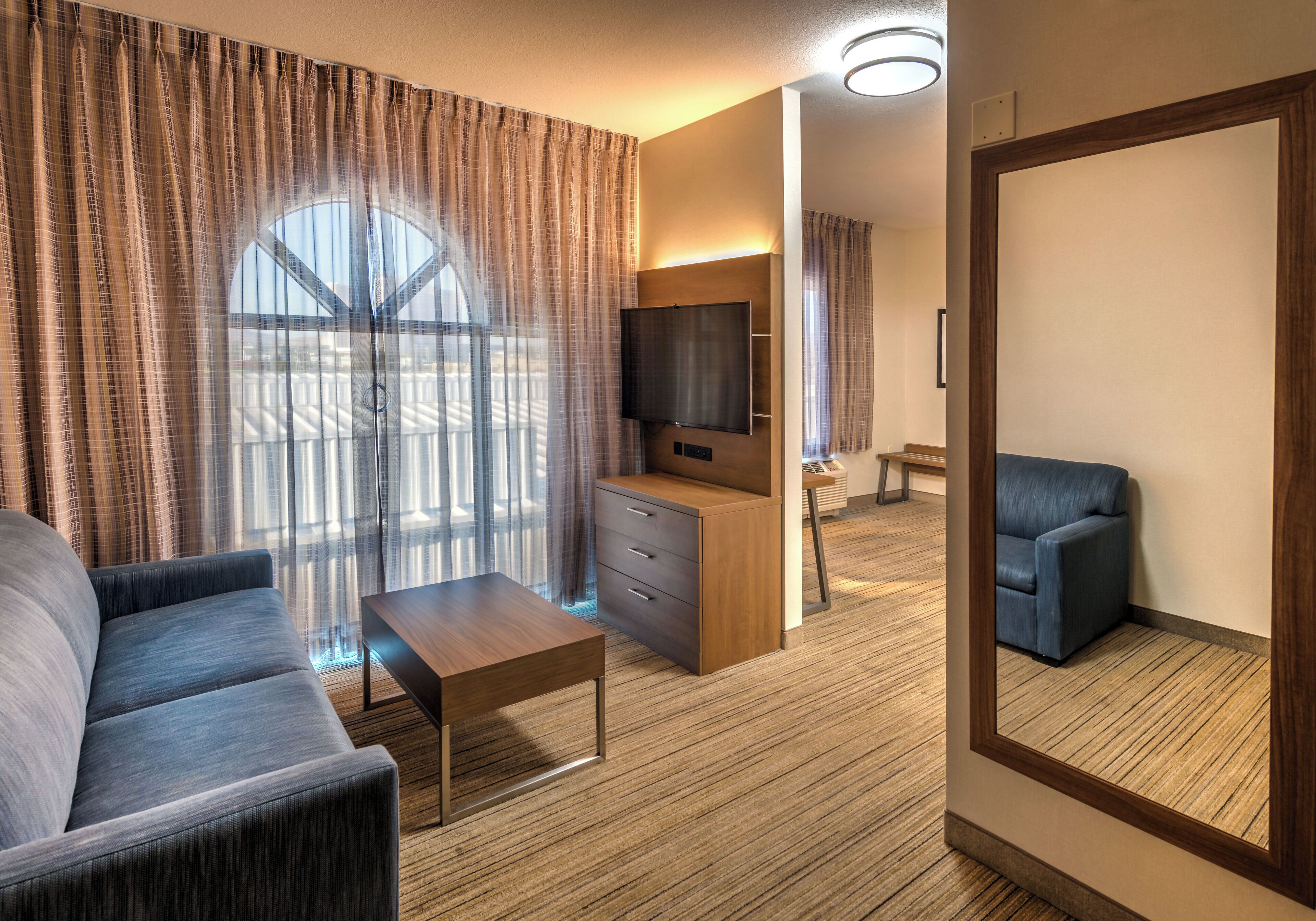 Habitación de hotel con sofá, mesa de centro, televisor y espejo.