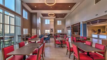 A spacious dining area with multiple tables and chairs, large windows, and a modern ceiling design.