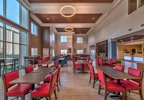A spacious dining area with multiple tables and chairs, large windows, and a modern ceiling design.