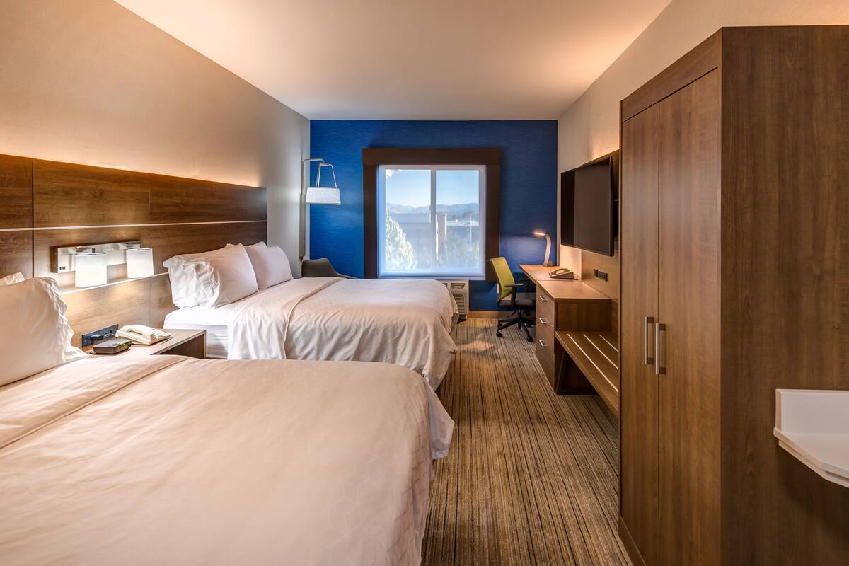 A hotel room with two beds, a desk, a TV, and a large wardrobe.