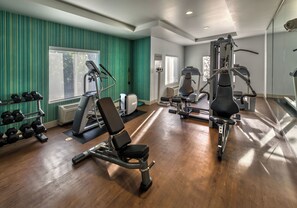 A gym with exercise equipment, a rack of dumbbells, and a window with a view of trees.