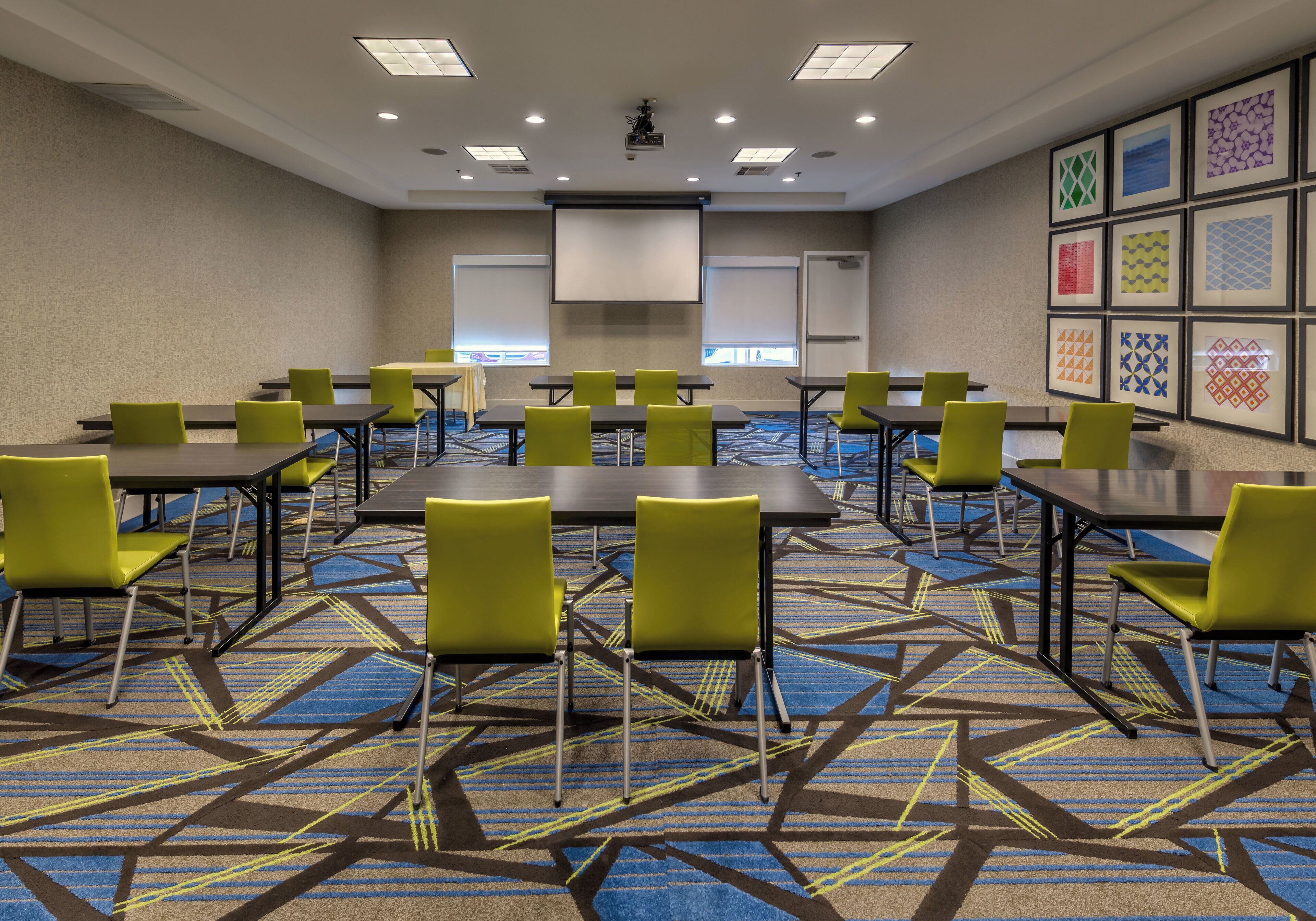 A conference room with tables and chairs, a projector, and framed artwork on the walls.