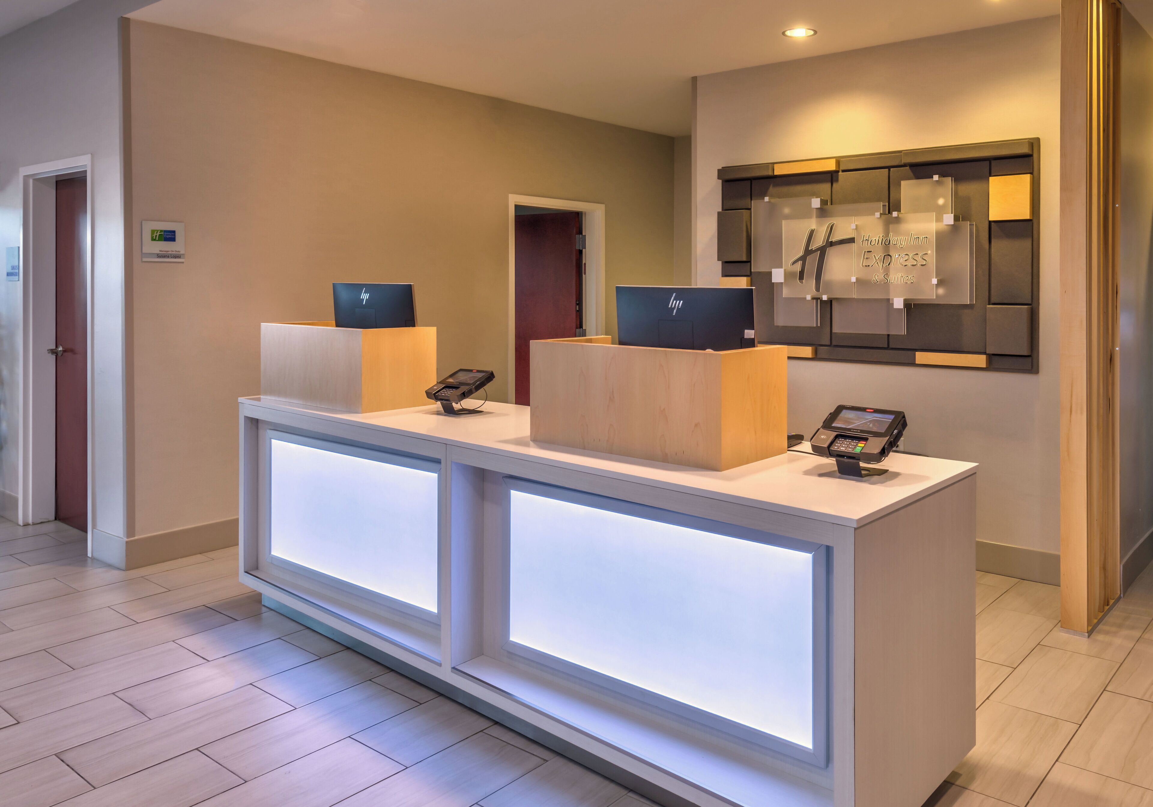 Un mostrador de recepción de hotel con dos computadoras portátiles HP, una pantalla digital y un letrero con el nombre del hotel.