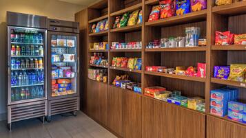 A vending machine stocked with various beverages and snacks, surrounded by shelves with packaged food items.