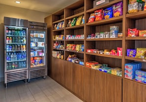 Una macchina distributrice piena di bevande e snack, circondata da scaffali con prodotti alimentari confezionati.