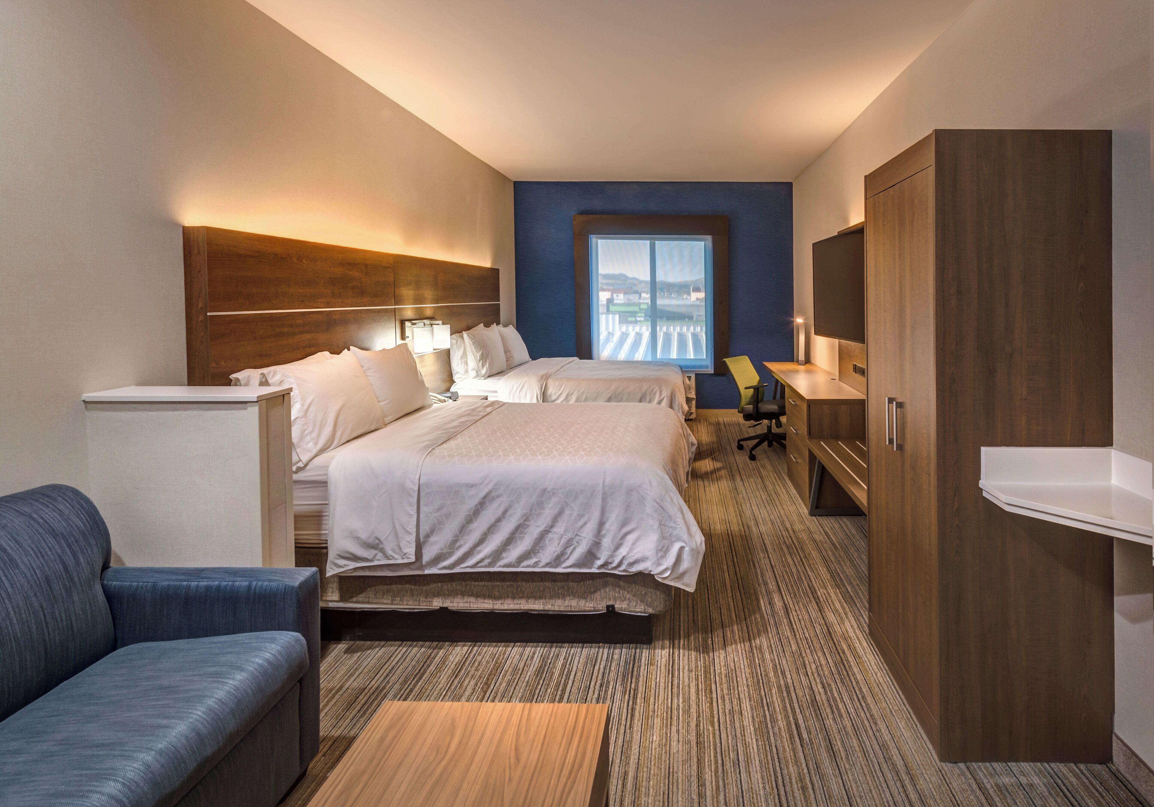 A hotel room with a large bed, a desk, a chair, a wardrobe, and a window with a view.