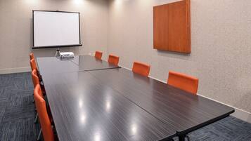 A conference room with a long table, six orange chairs, a projector, and a white screen on the wall.